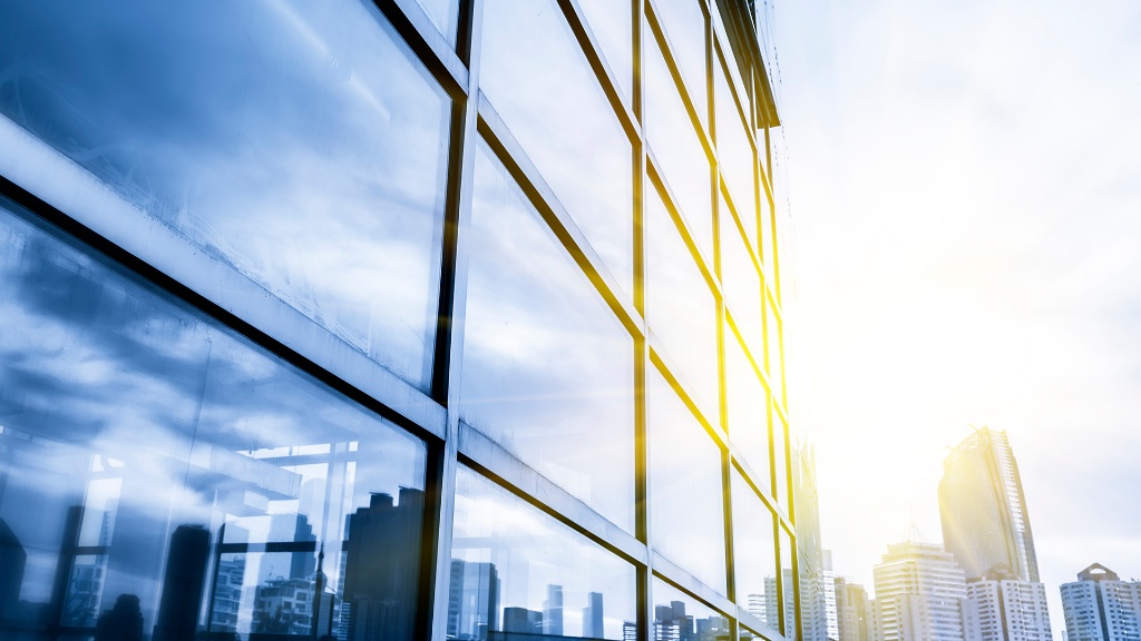 Glass curtain-wall building facade with gold sun reflections and cityscape — clarity of vision and executive leadership